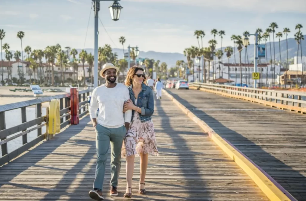 Casal caminhando no Stearns Wharf com o mar e palmeiras ao fundo