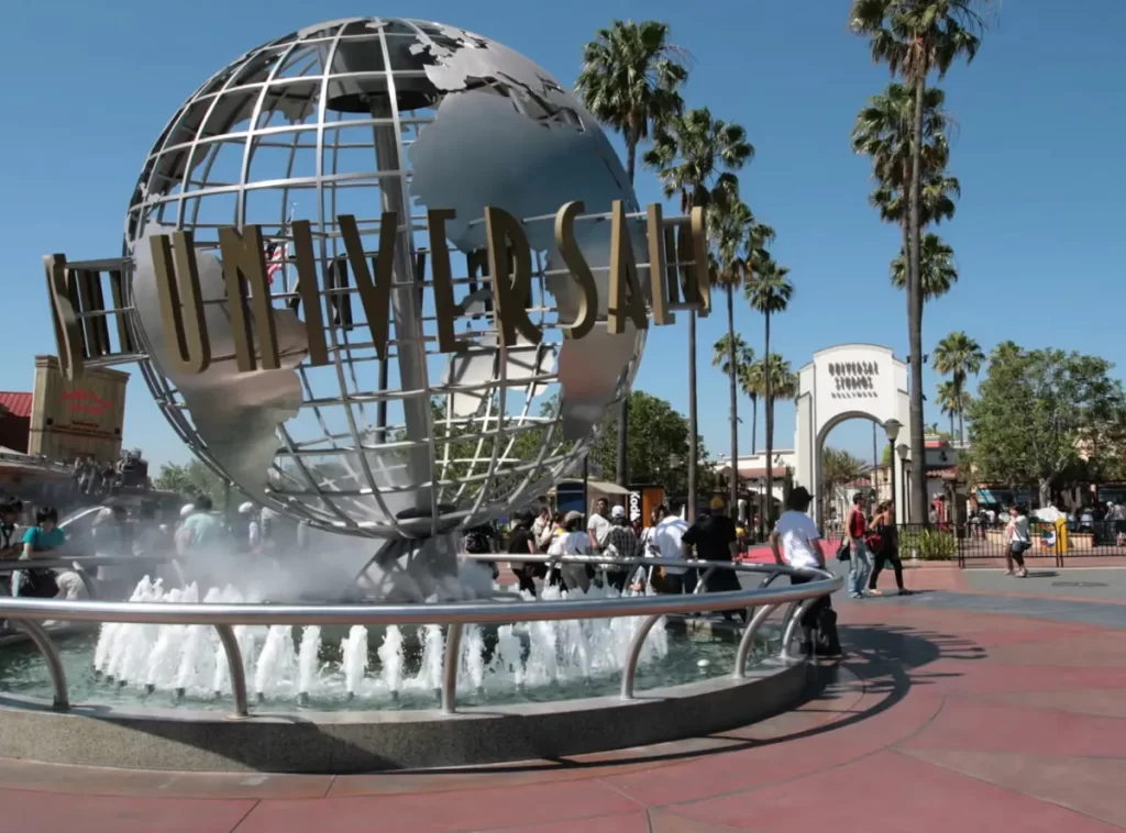 Entrada do Universal Studios Hollywood com globo giratório e turistas ao redor em dia ensolarado.