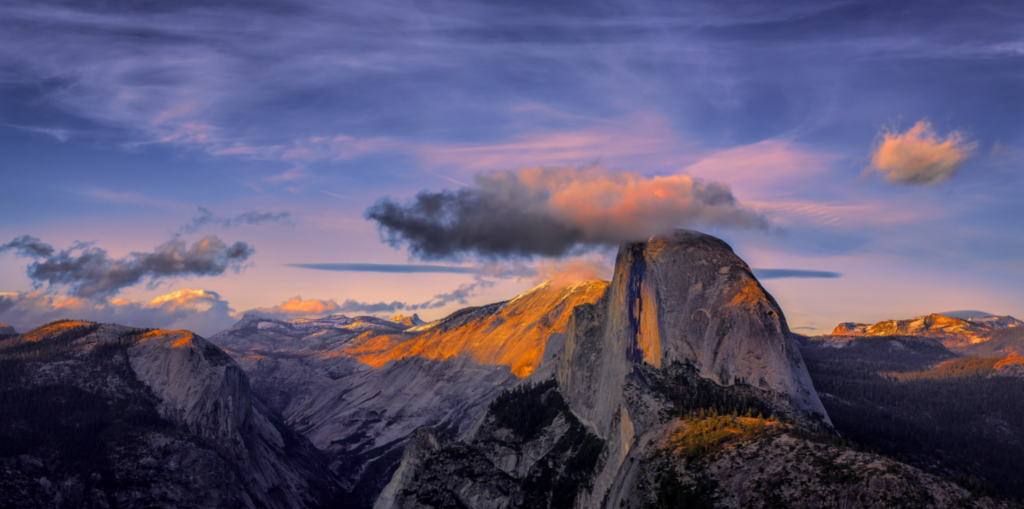 Half Dome iluminado pela luz dourada do pôr do sol com nuvens coloridas acima das montanhas.