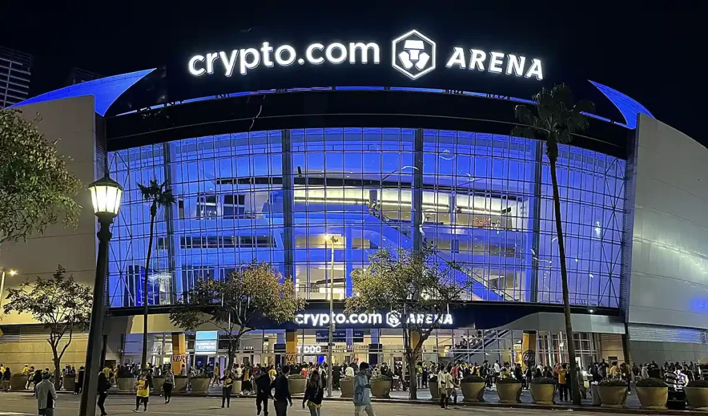 Crypto.com Arena, em Los Angeles, Califórnia, casa do Los Angeles Lakers na NBA. A fachada iluminada e a movimentação dos torcedores mostram a atmosfera de uma noite de basquete na cidade.