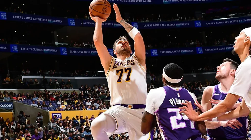 Momento de ação em uma partida do Los Angeles Lakers, com Lukla Doncic número 77 tentando finalizar uma jogada sob a marcação dos adversários. Um registro da intensidade do basquete da NBA.
