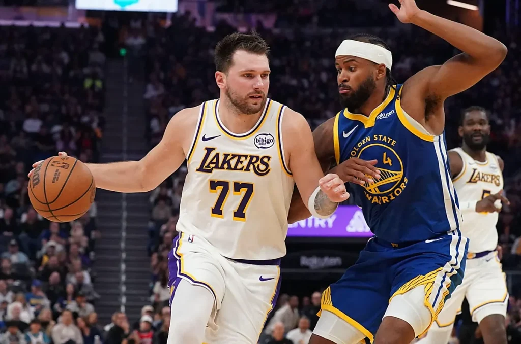 Jogos Lakers 2026 2027 - Lance de uma partida da NBA entre Los Angeles Lakers e Golden State Warriors, duas equipes da Conferência Oeste. A fotografia registra a disputa de bola em quadra, com a torcida ao fundo.