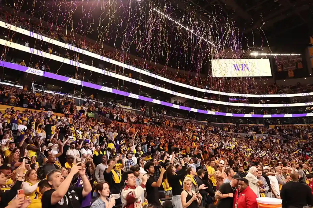 Celebração da torcida do Los Angeles Lakers na Crypto.com Arena, em Los Angeles. As arquibancadas lotadas e as fitas nas cores roxa e dourada mostram a energia de uma noite especial para os fãs da equipe.